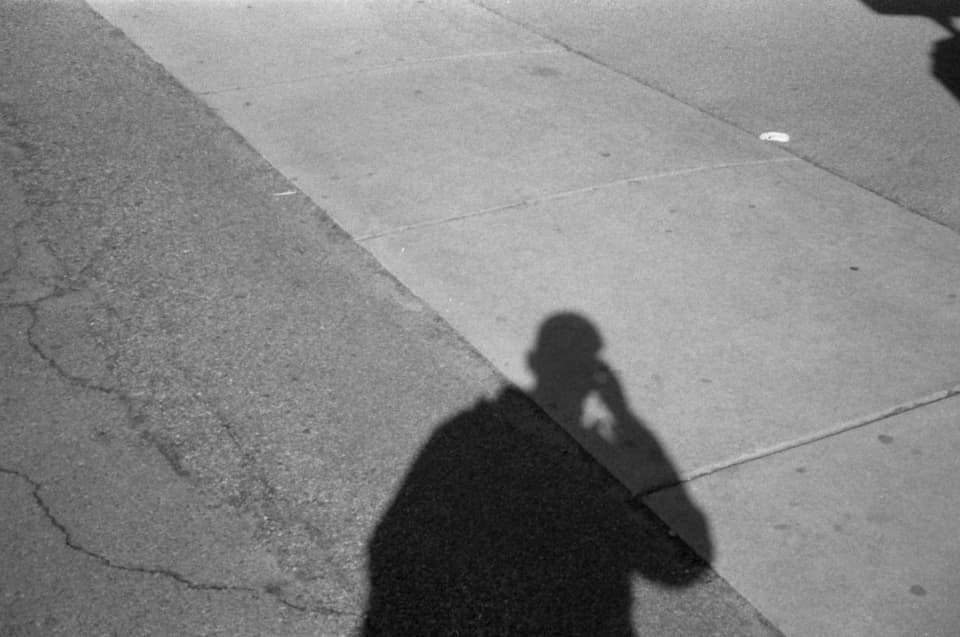 A single figure throwing a long shadow across a wall in low, warm sunlight